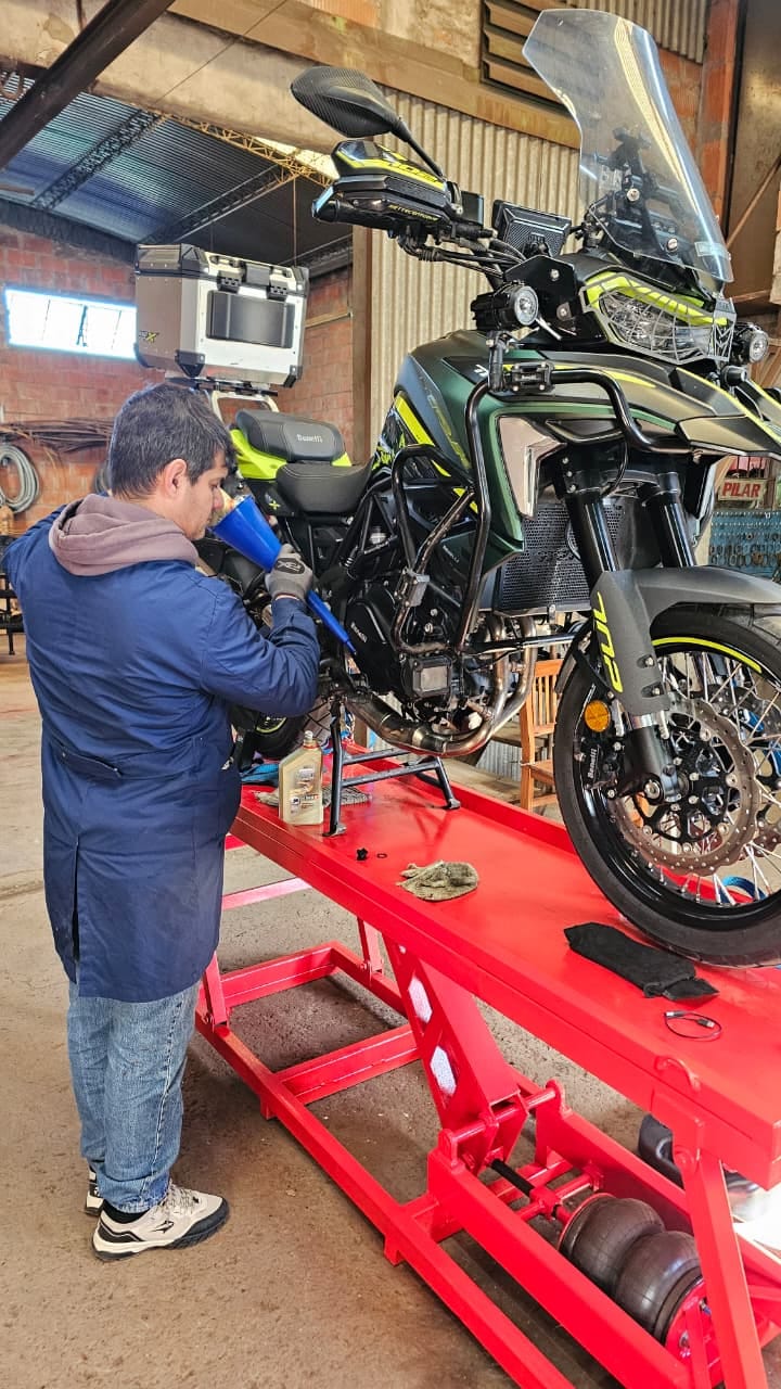 El dueño del taller haciendo el service de una moto en el elevador